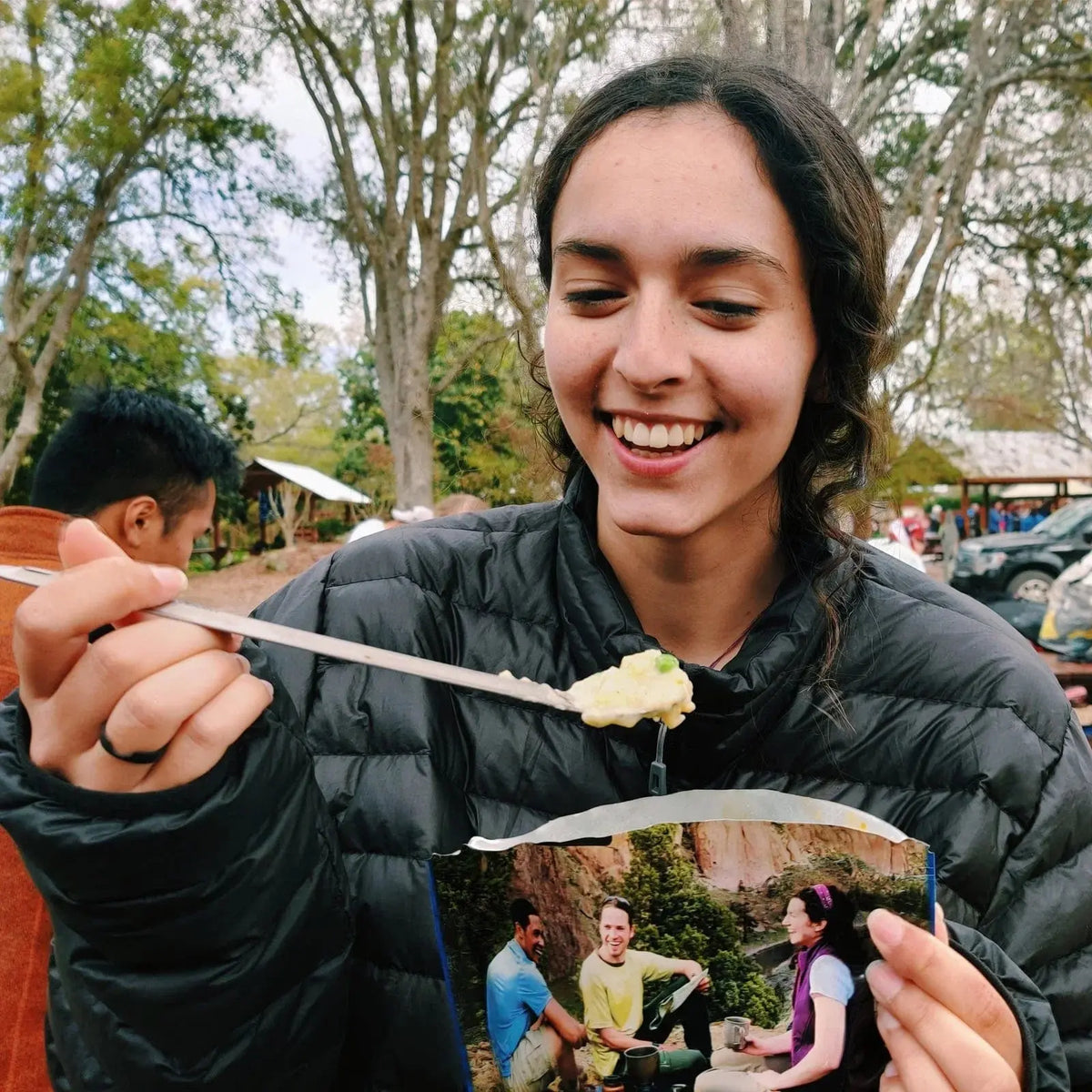 Person using SilverAnt Long Handle Titanium Spork outdoors, enjoying a meal in a camping setting.