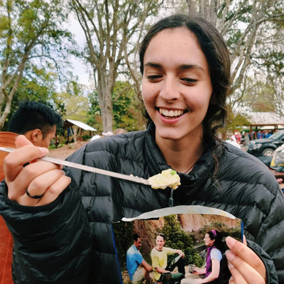 Person using SilverAnt Long Handle Titanium Spork outdoors, enjoying a meal in a camping setting.