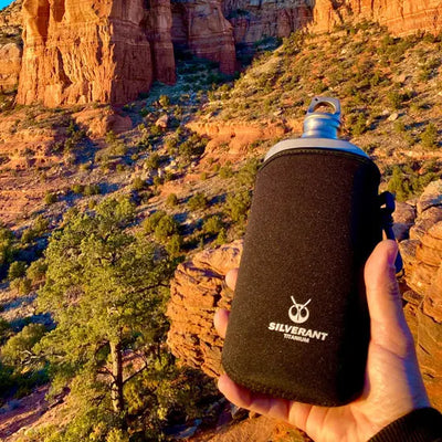 Person holding SilverAnt Ultralight Titanium Water Bottle Slim 27 oz 800 ml against scenic desert background.