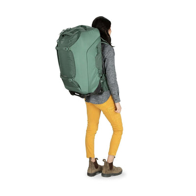 Osprey Sojourn Shuttle Wheeled Duffel 25"/60L in green, with oversized wheels and compression straps, displayed on a person for size reference.