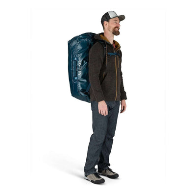 Man carrying Osprey Transporter Duffel 120, showcasing stowaway harness and rugged design, ideal for big trips and heavy gear travel.