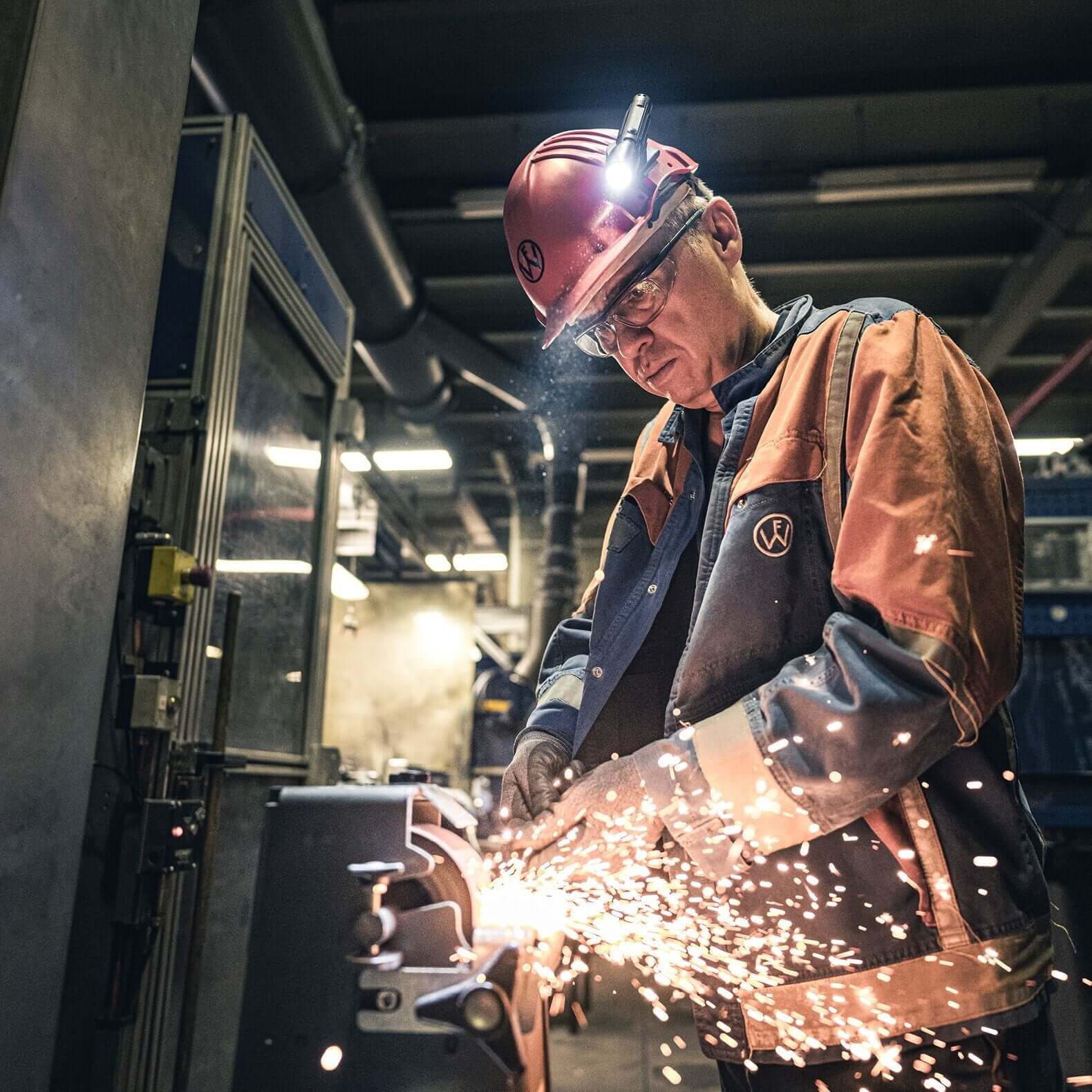 Worker wearing safety gear and headlamp while welding in an industrial workshop, creating sparks.