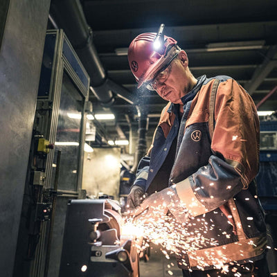 Worker wearing safety gear and headlamp while welding in an industrial workshop, creating sparks.