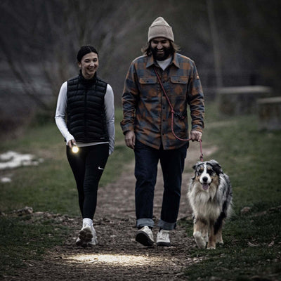 Couple walking a dog at dusk, using the P7R flashlight for better visibility on a trail.